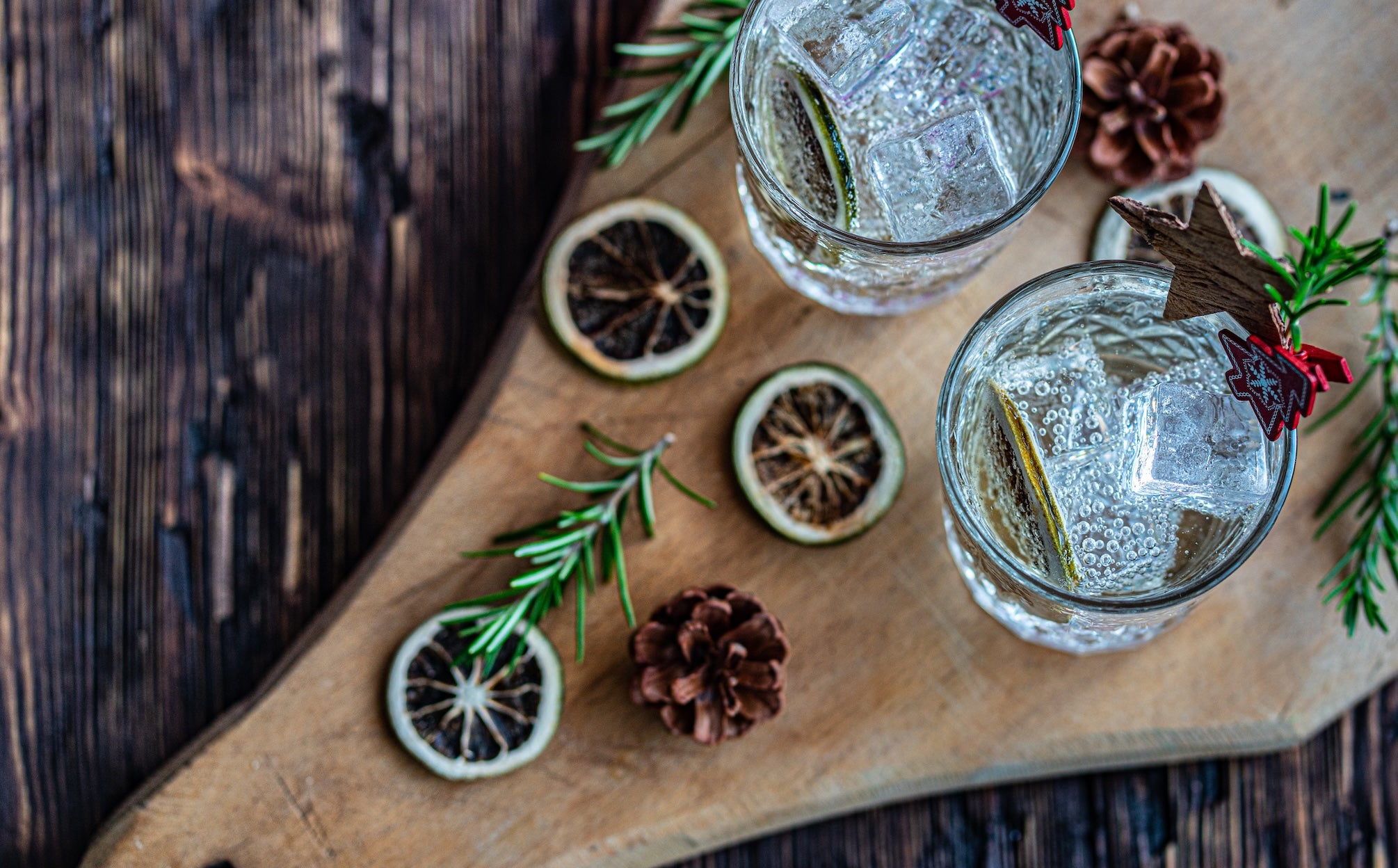 Two glasses of gin and tonic with lime slices and rosemary on a wooden board.